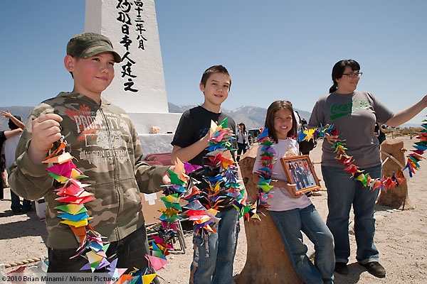Children pose behind the obelisk at the Manzanar cemetery, burial place of over one hundred prisoners who died at the former World War II concentration camp for Japanese Americans. The kids hold a string of origami cranes and a portrait of their grandmother who was unable to attend the annual pilgrimage.