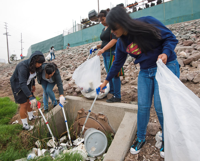 Four volunteers remove styrofoam and other waste from a drain on the bank of the stream.