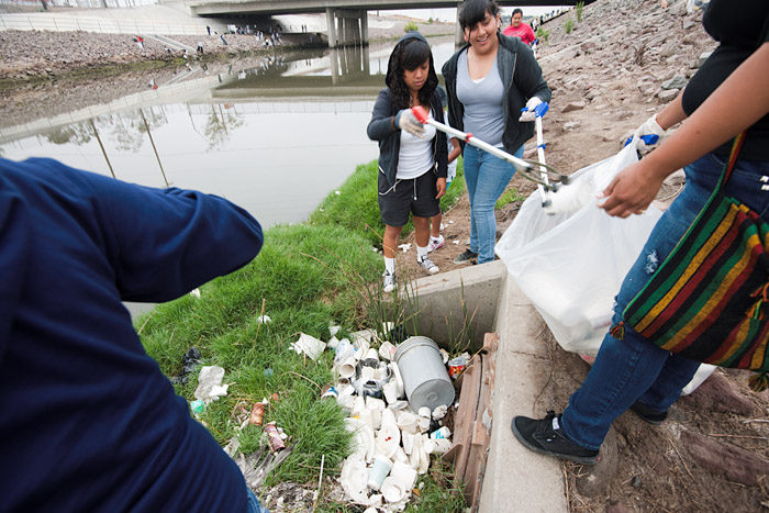 Four volunteers remove styrofoam and other waste from a drain on the bank of the stream. Most of the student volunteers are black or latino.