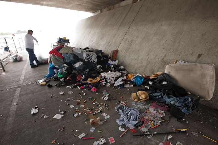 A volunteer begins removing old clothes and garbage from a homeless encampment on the bike path. The homeless population earlier was asked to remove any valuables from the area and was promised a meal if they helped remove the refuse.