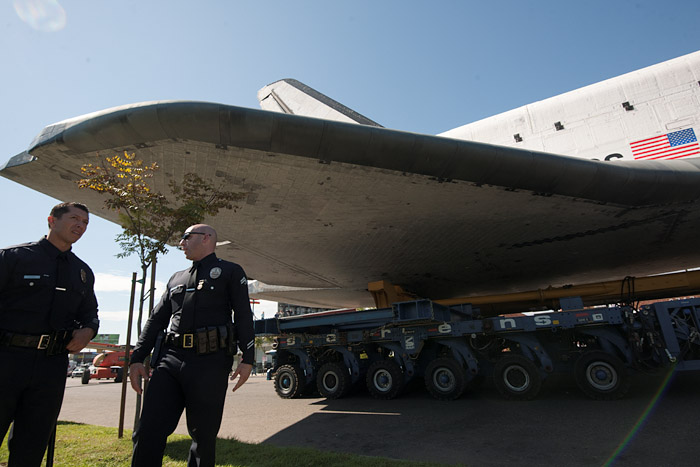 Endeavour's wing passes over juvenile trees and cops on the parkway bordering La Tijera Boulevard.